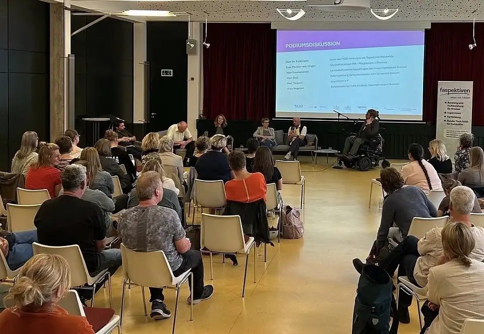 Blick von hintern durch die Teilnehmenden aufs Podium