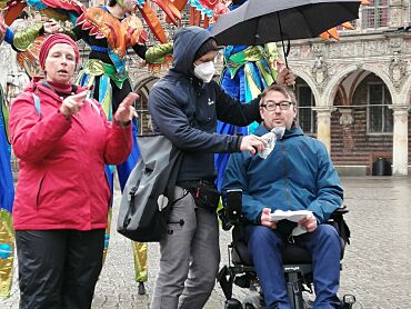 Arne Frankenstein bei seiner Rede mit seinem Assistenten und einer Gebärdensprachdolmetscherin. Es regnet, der Assistent hält einen Schirm.