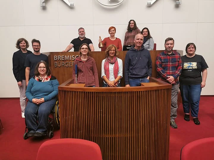 Gruppenbild der Teilnehmenden im Parlamentssaal vor und am Präsidentinnenpult