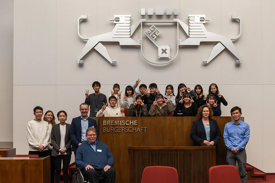 Gruppenbild der Schülergruppe, Andreas Conrads und Kai Steuck im Parlament am Präsidentinnenpult