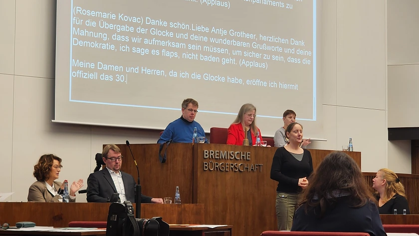 Frau Kovac eröffnet das Behindertenparlament. Sie sitzt zwischen 2 Personen auf dem Präsidentinnensitz der bremischen Bürgerschaft, Arne Frankenstein und Antje Grotheer sitzen daneben