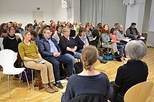 Das Foto zeigt die Teilnehmerinnen und Teilnehmer der Veranstaltung. Im Vordergrund sind zwei Gebärdendolmetscherin zu sehen. Sie sitzen zum Publikum hingewandt. 