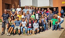 Auf dem Foto sind die Teilnehmerinnen und Teilnehmer an den World Dwarf Games sowie Angehörige abgebildet. Insgesamt zeigt das Gruppenfoto ca. 40 Personen in sommerlicher Freizeitbekleidung.