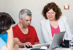 Ulrike Peter trägt ein pinkes Oberteil und eine weiße Jacke und schaut einem Durchblicker beim Testen am Laptop über die Schulter.