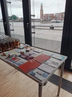 Ein Ständer mit Broschüren, im Hintergrund Blick auf den Hafen