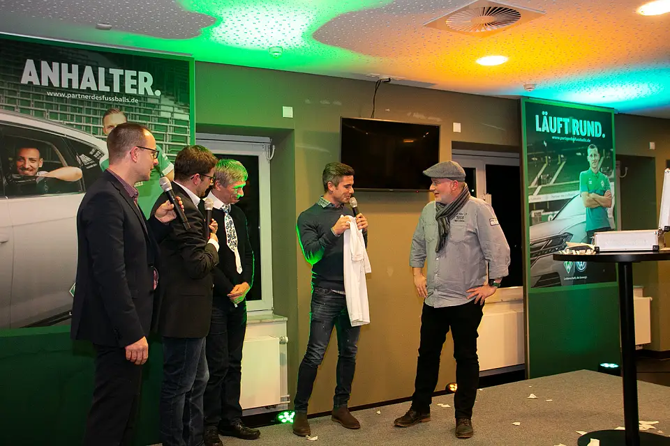 Fin Bartels &uuml;berreicht ein Trikot an Marco Bockholt. Die Moderatoren Kai Steuck und Kai Baumann sind ferner auf dem Bild mit dem Notar Wilhelm Winkelmeier zu sehen.